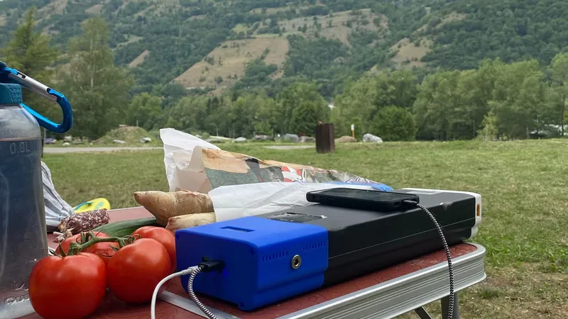 The finished power station charging a phone on a camping table, with an alpine valley behind it.